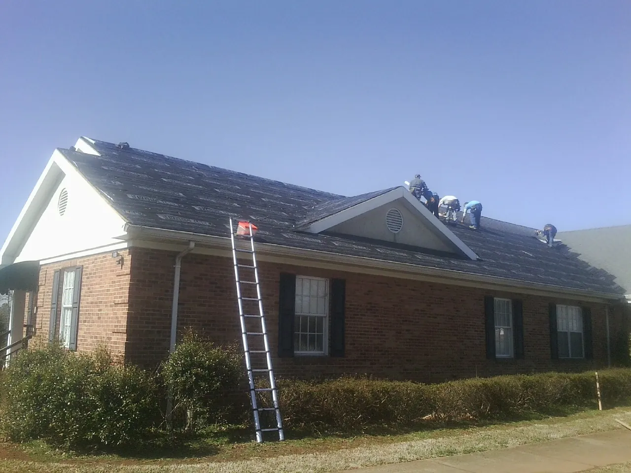 Crew tearing shingles off a brick ranch roof with a ladder set — Metal Roof Repair work by our crew in Kitzmiller