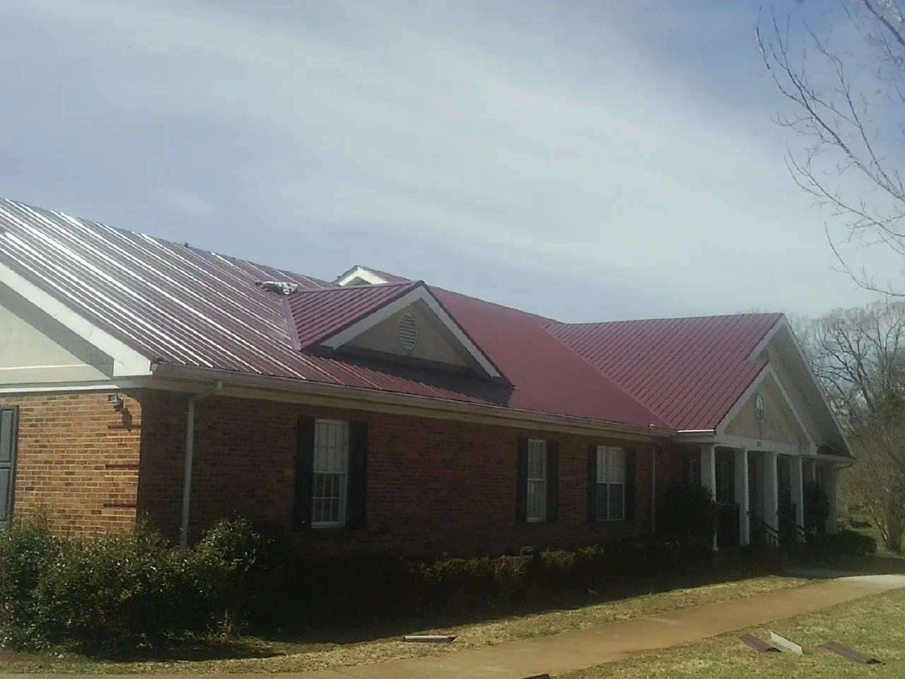 Red metal roof with gabled entries on a long brick building, from a Hail Damage Roof Repair job in Kitzmiller