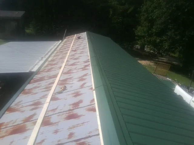 Old rusted panels beside newly installed green metal roofing — Wind Damage Roof Repair by Roofing Brothers in Kitzmiller