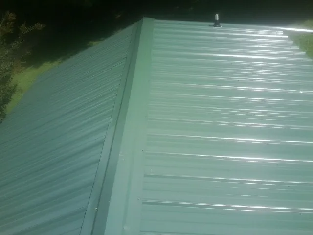 New green metal panels meeting at the ridge of a roof — Flat Roof Repair work by our crew in Kitzmiller