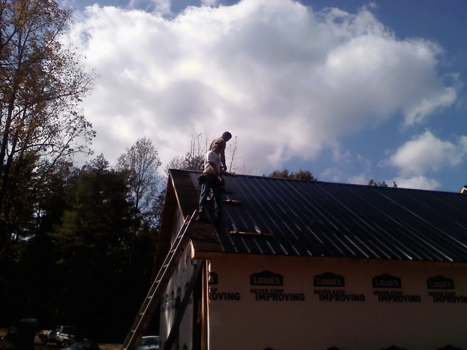 Roofer fastening dark metal panels high against a cloudy sky, from a Roof Inspection job in Kitzmiller